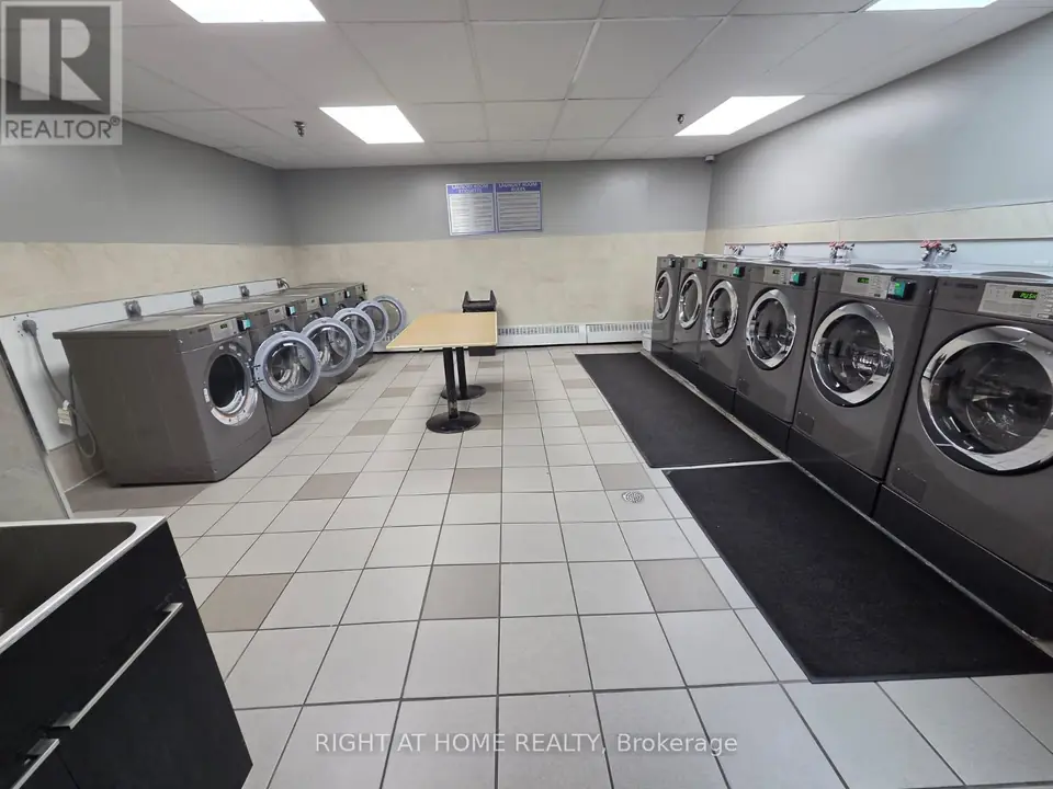 Shared laundry room with two rows of front-loading machines, a central table, a utility sink and a tiled floor.