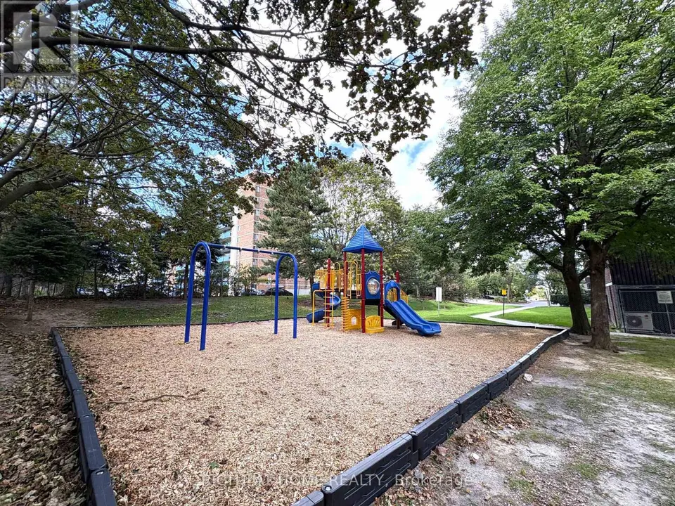 Outdoor playground with a blue swing set and a play structure with two slides on wood chips, surrounded by trees.